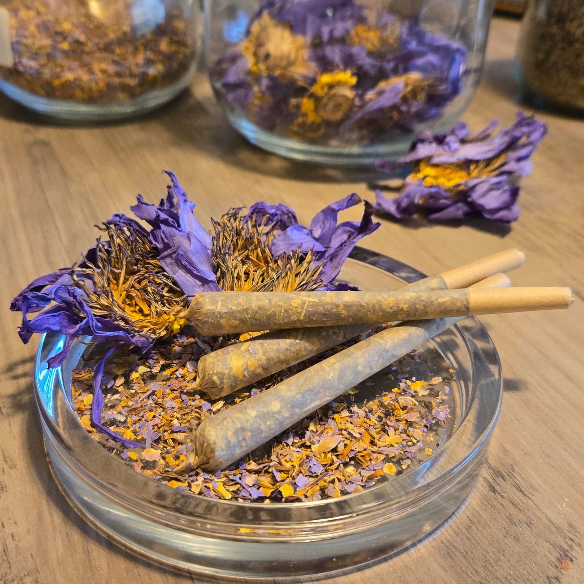 Three Astral Herbal pre rolls on a glass jar filled with dried blue lotus petals