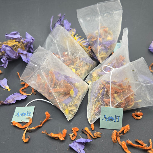 Astral Herbal tea bags with wild dagga, blue lotus, and chamomile on a black background with loose blue lotus and wild dagga petals in the foreground.