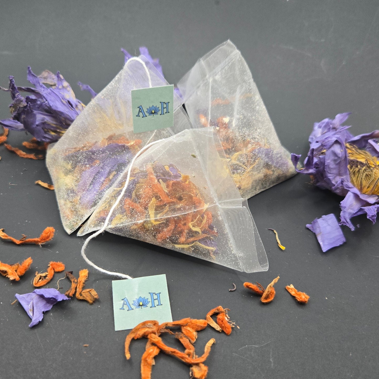 Astral Herbal tea bags with wild dagga, blue lotus, and chamomile on a black background with loose blue lotus and wild dagga petals in the foreground.
