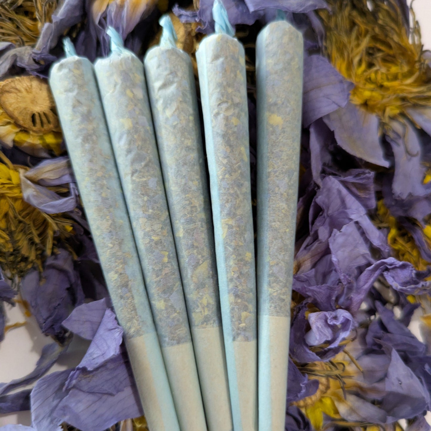 blue lotus pre rolls stacked on top of whole blue lotus flowers by Astral Herbal