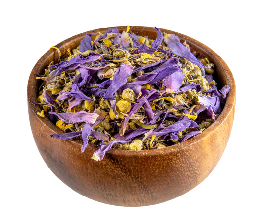 Wooden bowl filled with dried purple and green herbs on a white background