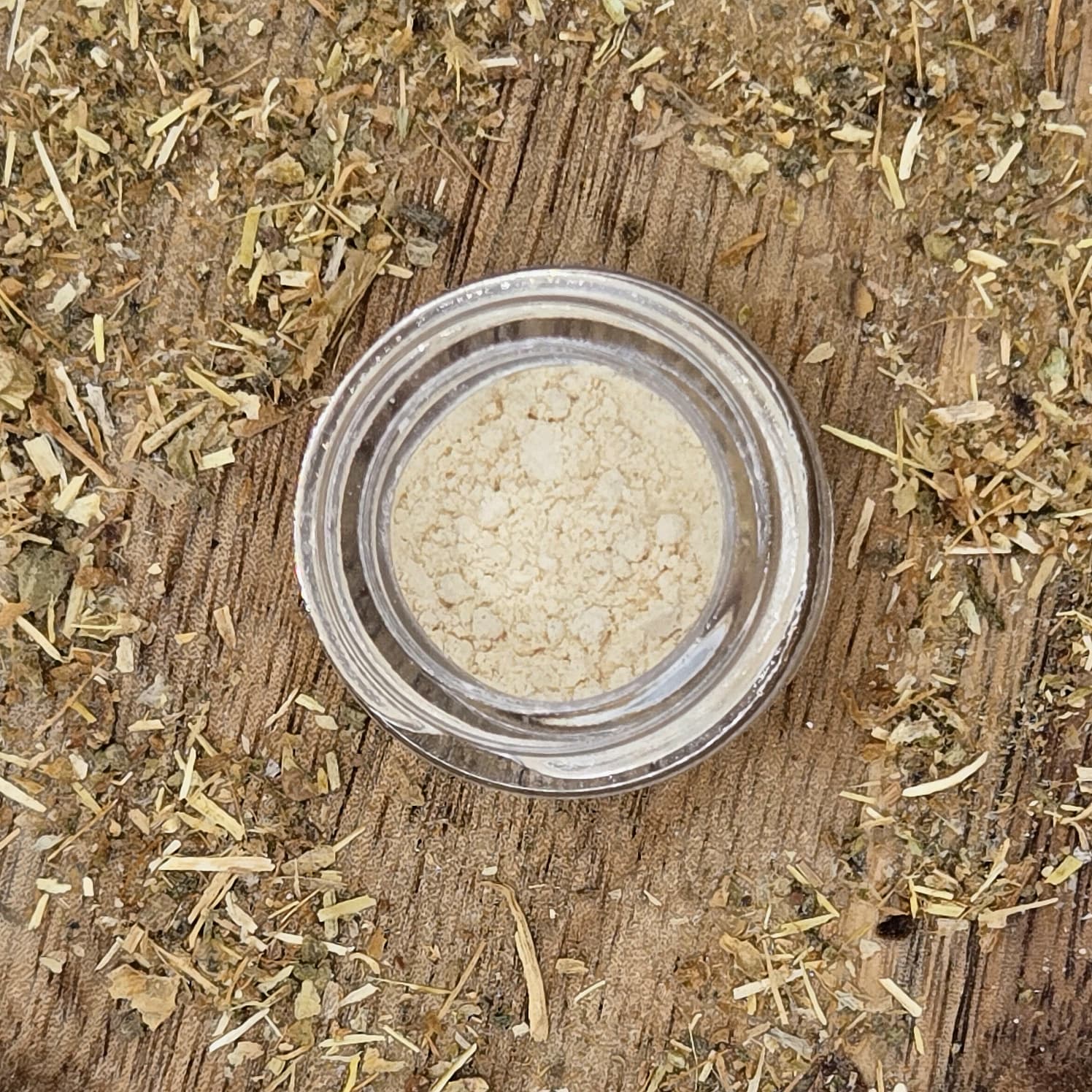 Kanna extract MT-55 in a glass jar on a wooden surface with a background of fermented kanna by Astral Herbal.